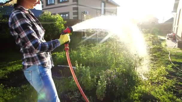 Young woman watering plants in her garden with garden hose. Hobby concept — Stock Video