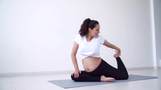 Hälsobegreppet. Ung gravid kvinna tränar yoga i det vita rummet — Stockvideo