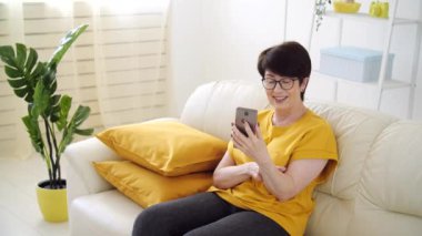 Kişisel izolasyon kavramı. Oturma odasındaki koltukta oturan orta yaşlı bir kadın video aracılığıyla konuşuyor..