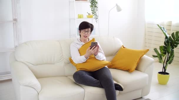 Koncept sebeizolace. Žena středního věku sedí na pohovce v obývacím pokoji a mluví prostřednictvím videohovoru. — Stock video