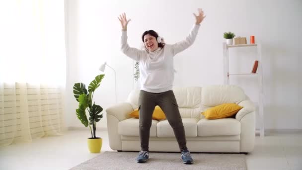 Вихідні вдома концепція. Щаслива жінка слухає музику і танцює у вітальні — стокове відео
