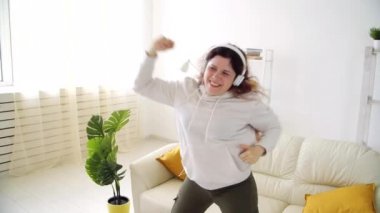 Ev kavramında hafta sonu. Oturma odasında müzik dinleyip dans eden mutlu bir kadın.
