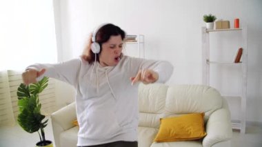 Ev kavramında hafta sonu. Oturma odasında müzik dinleyip dans eden mutlu bir kadın.