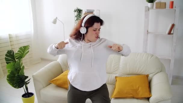 Helg på hemmaplan. Glad kvinna lyssnar på musik och dansar i vardagsrummet — Stockvideo