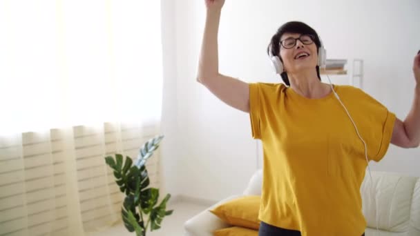 Gyönyörű idős nő nyugodt és táncol, zenét hallgat otthon. — Stock videók