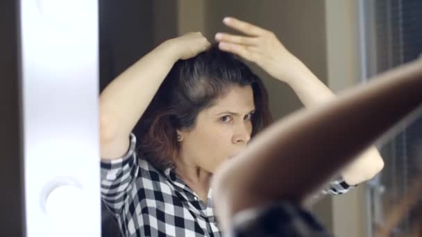 Joven mujer frustrada se mira en el espejo y le arranca un pelo gris de la cabeza. Concepto de foto de una mujer joven envejeciendo — Vídeo de stock