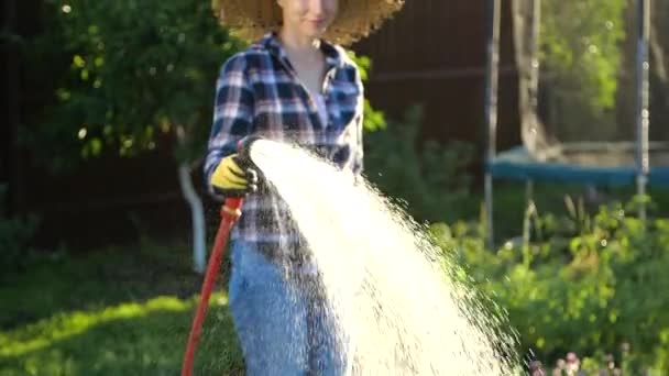 Jonge vrouw besproeit planten in haar tuin met tuinslang. Hobby-concept — Stockvideo