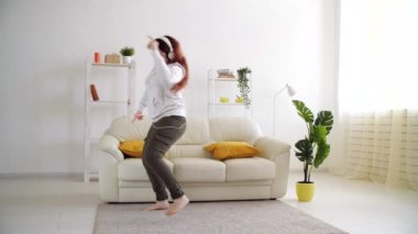 Oturma odasında müzik dinleyip dans eden mutlu bir kadın.