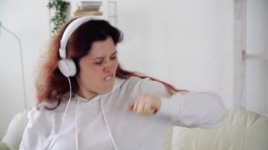 Oturma odasında müzik dinleyip dans eden mutlu bir kadın.