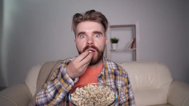 Domácí kino a televizní koncept. Šokovaný a vystrašený muž se dívá na televizi a jí popcorn — Stock video