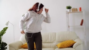 Ev kavramında hafta sonu. Oturma odasında müzik dinleyip dans eden mutlu bir kadın.