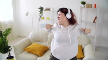 Ev kavramında hafta sonu. Oturma odasında müzik dinleyip dans eden mutlu bir kadın.