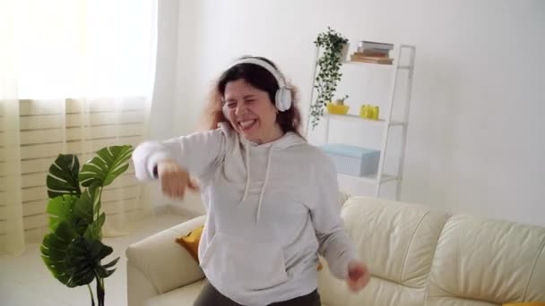 Hétvége otthon koncepció. Boldog nő zenét hallgat és táncol a nappaliban — Stock videók