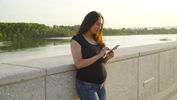 Mladá těhotná žena pomocí chytrého telefonu stojící v parku — Stock video