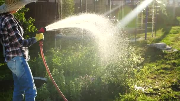 Mujer joven regando plantas en su jardín con manguera de jardín. Concepto Hobby — Vídeo de stock