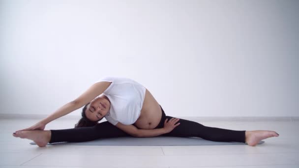 Концепция здоровья. Молодая беременная женщина занимается йогой в белой комнате — стоковое видео