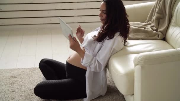 Νεαρή έγκυος γυναίκα στο σπίτι κοιτάζοντας έναν υπολογιστή ταμπλέτας — Αρχείο Βίντεο