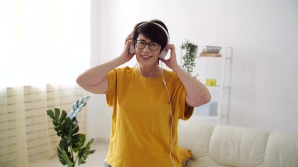 Mulher sênior bonita relaxada e dançando, ouvindo música em casa . — Vídeo de Stock