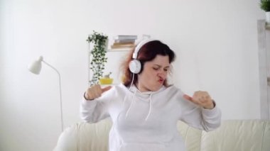 Oturma odasında müzik dinleyip dans eden mutlu bir kadın.