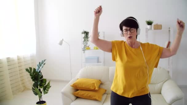 Mulher sênior bonita relaxada e dançando, ouvindo música em casa . — Vídeo de Stock