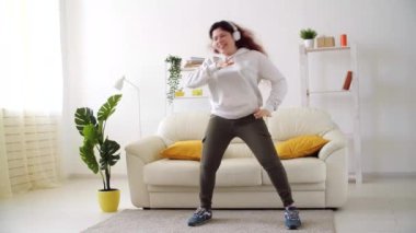 Ev kavramında hafta sonu. Oturma odasında müzik dinleyip dans eden mutlu bir kadın.