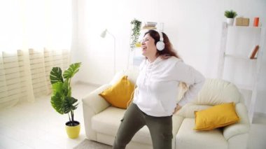 Ev kavramında hafta sonu. Oturma odasında müzik dinleyip dans eden mutlu bir kadın.