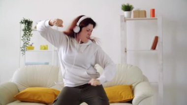 Oturma odasında müzik dinleyip dans eden mutlu bir kadın.
