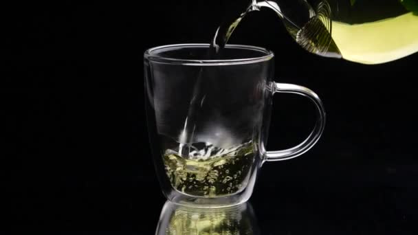 Té verde se vierte desde la tetera de vidrio un fondo negro — Vídeos de Stock