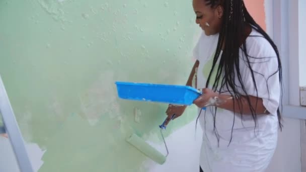 Концепция реконструкции квартир. Улыбающаяся афроамериканка перекрашивает свой дом, держа в руках краску, покрытую оранжевой и зеленой краской — стоковое видео