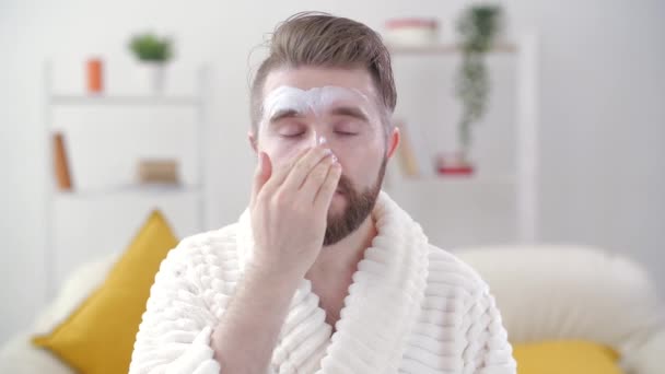 Skin treatment and selfcare concept. Handsome young man applying cream to his face at home — Stock Video