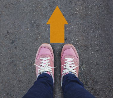 Asfalt bir yolda duran sarı oklu bir çift ayakkabı..