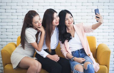 Mutlu anılar. Kanepede oturan üç genç ve mutlu bayan arkadaş telefonla selfie çekiyorlar..