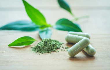 Tahtanın üzerinde yeşil bitkisel yaprak olan bitki kapsülü, Andrographis paniklemiş bitkisel antipiretik kapsüller..