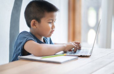 Asyalı çocuk evde dijital tabletle online eğitim öğreniyor ve okul ödevi yapıyor. İnternet, e-öğrenim çevrimiçi eğitim hakkında bilgi aramak için tablet kullanan çocuk.