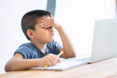 Üzgün Asyalı çocuk evde dijital tabletle online eğitim öğreniyor ve okul ödevi yapıyor. İnternet, e-öğrenim çevrimiçi eğitim hakkında bilgi aramak için tablet kullanan çocuk.