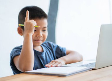 Asyalı çocuk evde dijital tabletle online eğitim öğreniyor ve okul ödevi yapıyor. İnternet, e-öğrenim çevrimiçi eğitim hakkında bilgi aramak için tablet kullanan çocuk.