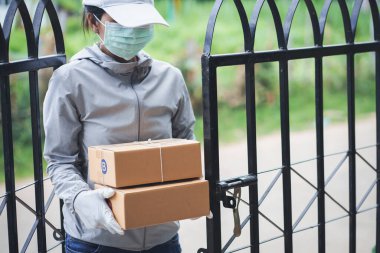 Elinde alışveriş kutusu, tıbbi lastik eldiven ve maskeli teslimat paketleri olan teslimatçı kadın. Çevrimiçi alışveriş ve ekspres teslimat