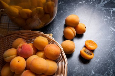 Tatlı Kayısı Kompostosu karanlık mermer üzerinde büyük cam kavanoz konserve ve yaz anda olgun organik kayısı hasat. Rustik tarzı - organik sarı sulu kayısı bütün ve yarıya sarı ahşap sepet ve ev yapımı Kayısı Kompostosu canne kompozisyon