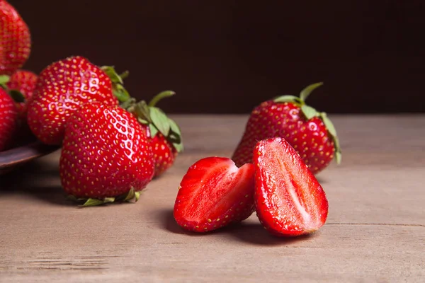 Tatlı çilek ile dilimlenmiş yarım ve bütün antika arka plan üzerinde meyve. Ahşap arka plan üzerinde çilek taze Olgun kırmızı meyveler ile kil plaka