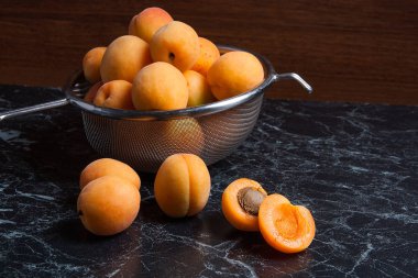 Olgun organik kayısı çelik kevgir içinde. Kompozisyon rustik tarzı - çelik kevgir içinde organik sarı sulu kayısı ve karanlık mermer zemin üzerine bütün ve yarıya kayısı. Sağlıklı gıda kavramı. Hasat zamanı