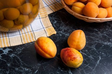 Tatlı Kayısı Kompostosu karanlık mermer üzerinde büyük cam kavanoz konserve ve yaz anda olgun organik kayısı hasat. Rustik tarzı - organik sarı sulu kayısı bütün ve yarıya sarı ahşap sepet ve ev yapımı Kayısı Kompostosu canne kompozisyon