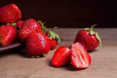 Tatlı çilek ile dilimlenmiş yarım ve bütün antika arka plan üzerinde meyve. Ahşap arka plan üzerinde çilek taze Olgun kırmızı meyveler ile kil plaka