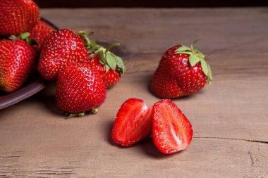 Tatlı çilek ile dilimlenmiş yarım ve bütün antika arka plan üzerinde meyve. Ahşap arka plan üzerinde çilek taze Olgun kırmızı meyveler ile kil plaka