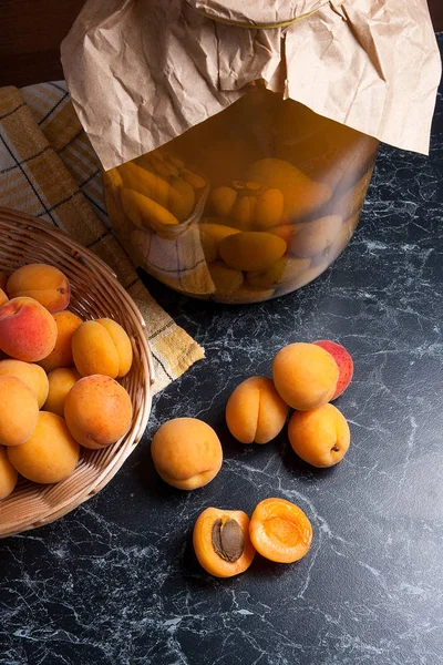 Tatlı Kayısı Kompostosu karanlık mermer üzerinde büyük cam kavanoz konserve ve yaz anda olgun organik kayısı hasat. Rustik tarzı - organik sarı sulu kayısı bütün ve yarıya sarı ahşap sepet ve ev yapımı Kayısı Kompostosu canne kompozisyon