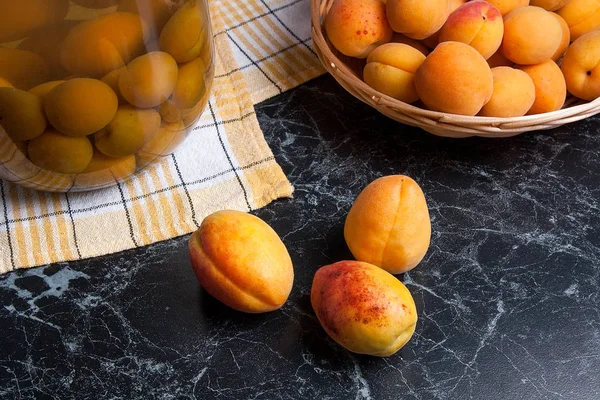 Tatlı Kayısı Kompostosu karanlık mermer üzerinde büyük cam kavanoz konserve ve yaz anda olgun organik kayısı hasat. Rustik tarzı - organik sarı sulu kayısı bütün ve yarıya sarı ahşap sepet ve ev yapımı Kayısı Kompostosu canne kompozisyon