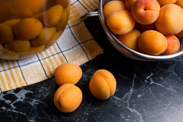 Tatlı Kayısı Kompostosu karanlık mermer üzerinde büyük cam kavanoz konserve ve yaz anda olgun organik kayısı hasat. Rustik tarzı - organik sarı sulu kayısı bütün ve çelik kevgir ve ev yapımı Kayısı Kompostosu b konserve yarıya kompozisyon