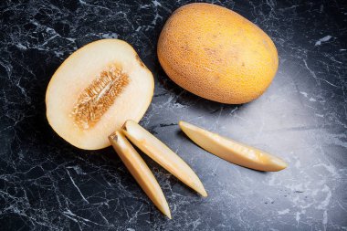 Olgun bütün ve yaz saati yarım honeydew kavun meyve. Olgun sulu kavun meyve karanlık mermer arka plan üzerine dilimlenmiş
