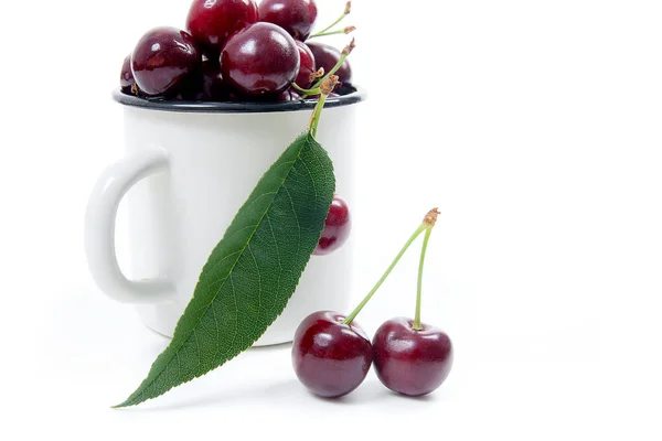 White cup with ripe berries of red sweet cherry and several berries in front of the cup. Composition on a white background
