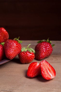 Tatlı çilek ile dilimlenmiş yarım ve bütün antika arka plan üzerinde meyve. Ahşap arka plan üzerinde çilek taze Olgun kırmızı meyveler ile kil plaka
