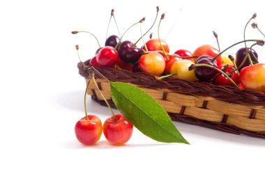 Sepet beyaz adam üzerinde kiraz ağacının yaprak yeşil ile sarı ve kırmızı tatlı kiraz ve birkaç sarı meyve olgun çilek ile